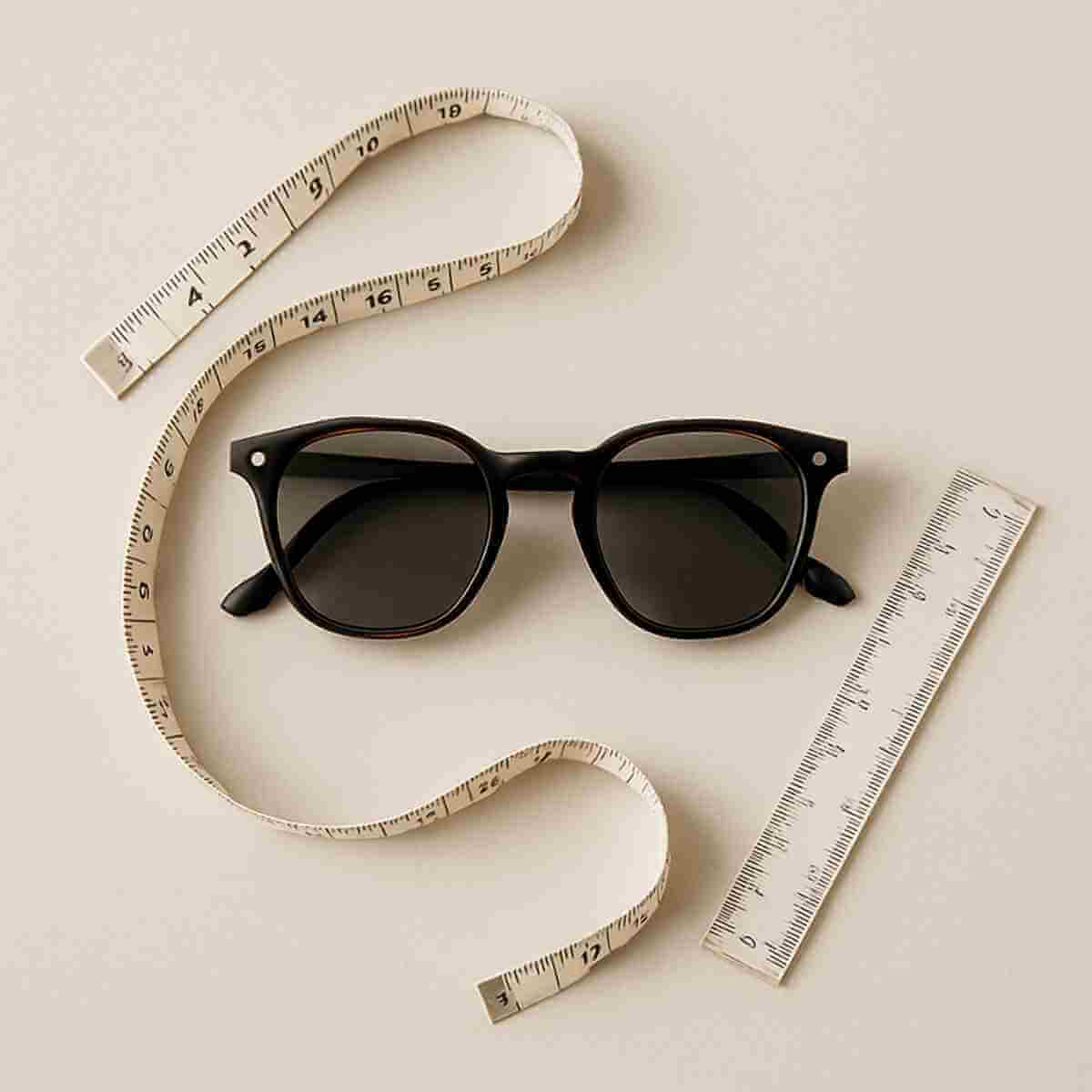Flat lay with sunglasses and measuring tape illustrating lens width for small faces in a petite size guide
