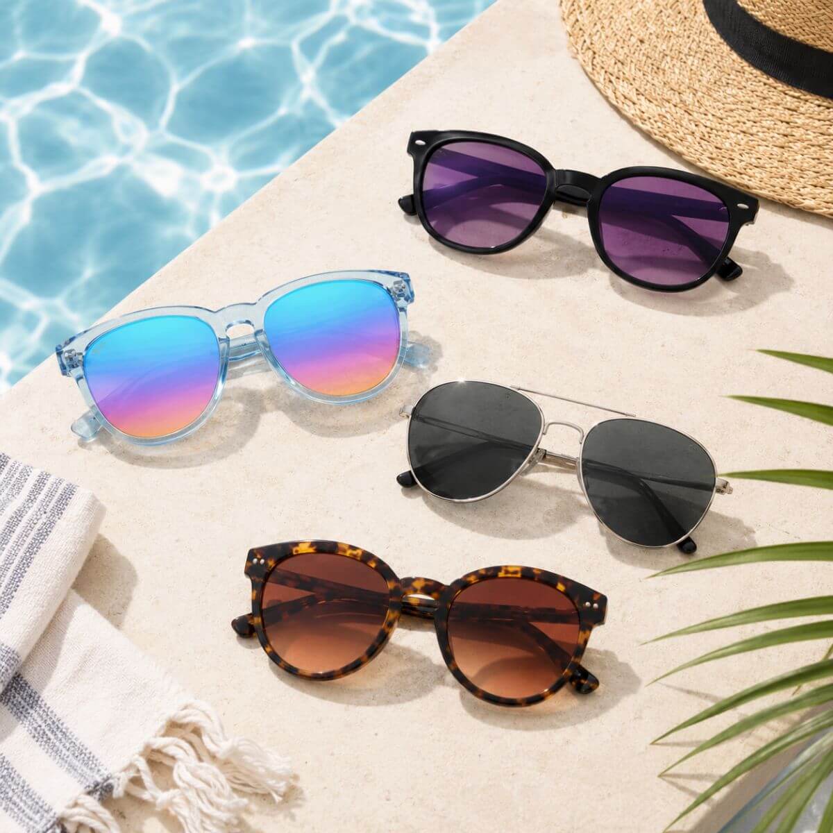 Poolside flat lay of aviator, round, and rectangular sunglasses arranged beside a swimming pool with a straw hat and beach towel