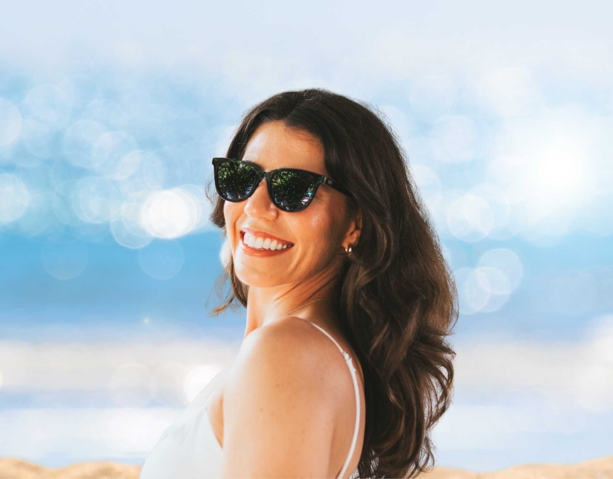 Woman wearing black Half Moon Bay cat eye sunglasses at the beach, cat eye sunglasses for smaller face and petite features, lightweight polarized summer eyewear.