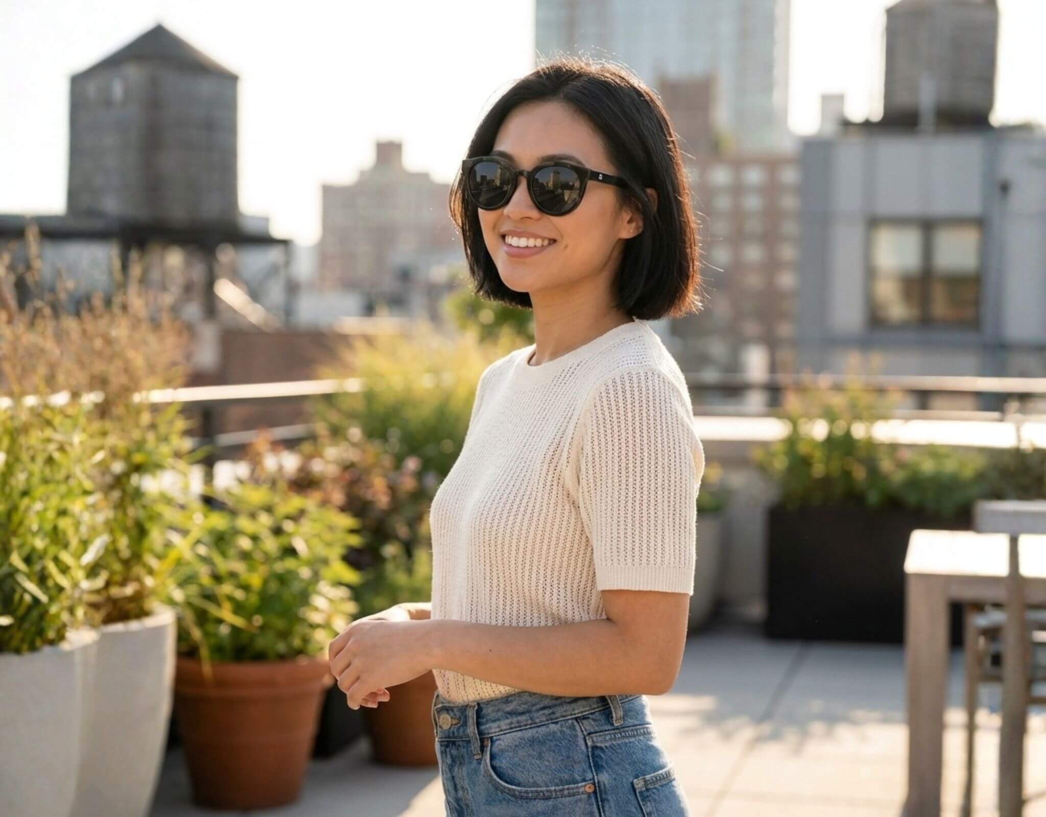 Small sunglasses for small faces worn by woman in Bar Harbor black frame with grey lenses on a sunny rooftop, designed for petite features and small head by ello sunglasses