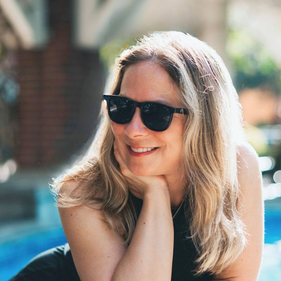Smiling woman wearing black and grey sunglasses for petite faces, styled casually outdoors.