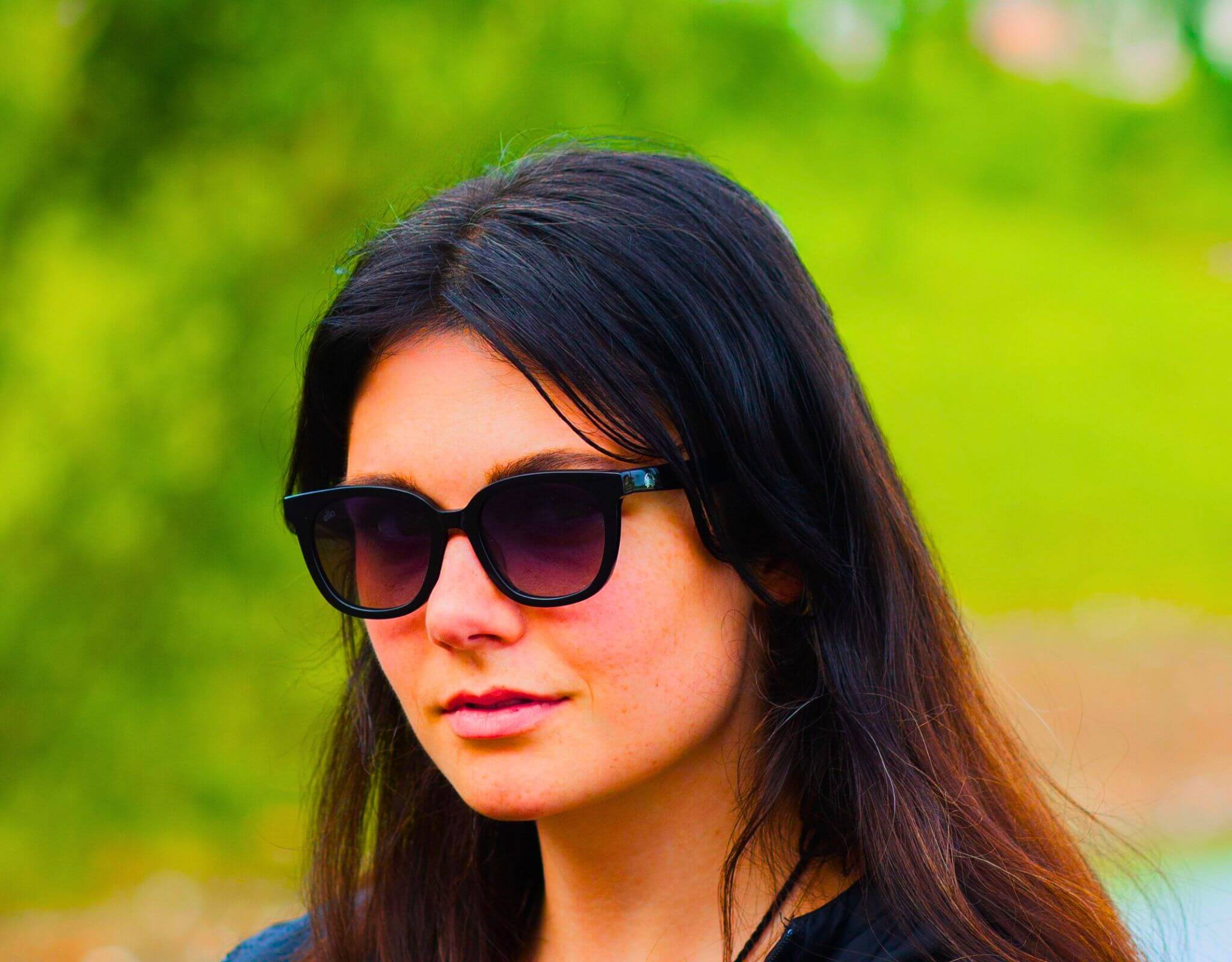 Confident woman wearing black lavender Pebble Beach sunglasses for little faces in a sunny park setting.