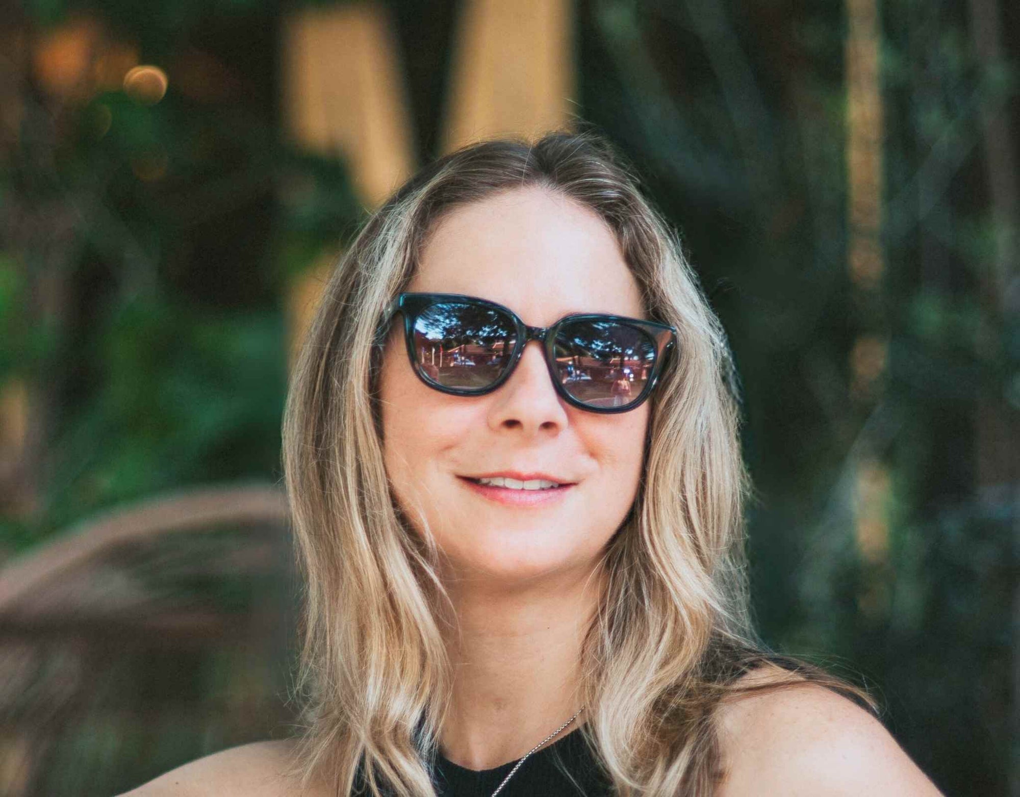 Confident woman wearing black lavender Pebble Beach sunglasses for little faces in a sunny park setting.