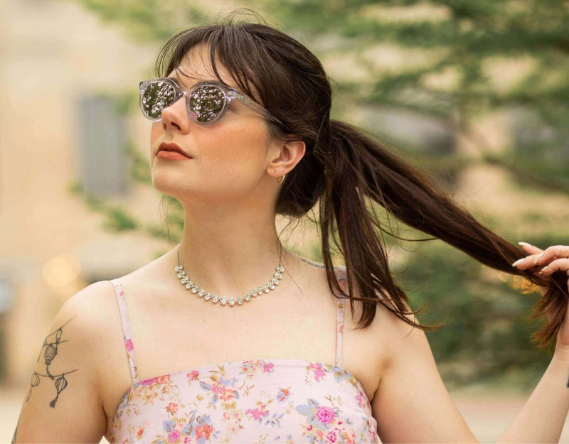 Clear purple Bar Harbor small sunglasses for small faces shown on a woman in a floral dress outdoors