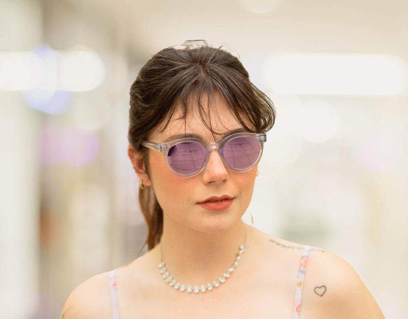 Clear purple Bar Harbor small sunglasses for small faces shown on a woman in a blurred outdoor backdrop