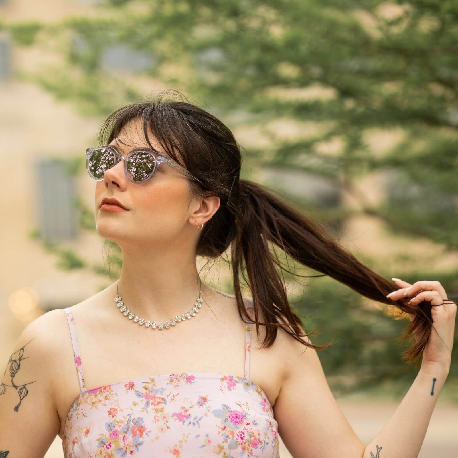 Woman wearing clear lavender sunglasses for petite faces, styled with a floral dress and ponytail outdoors.