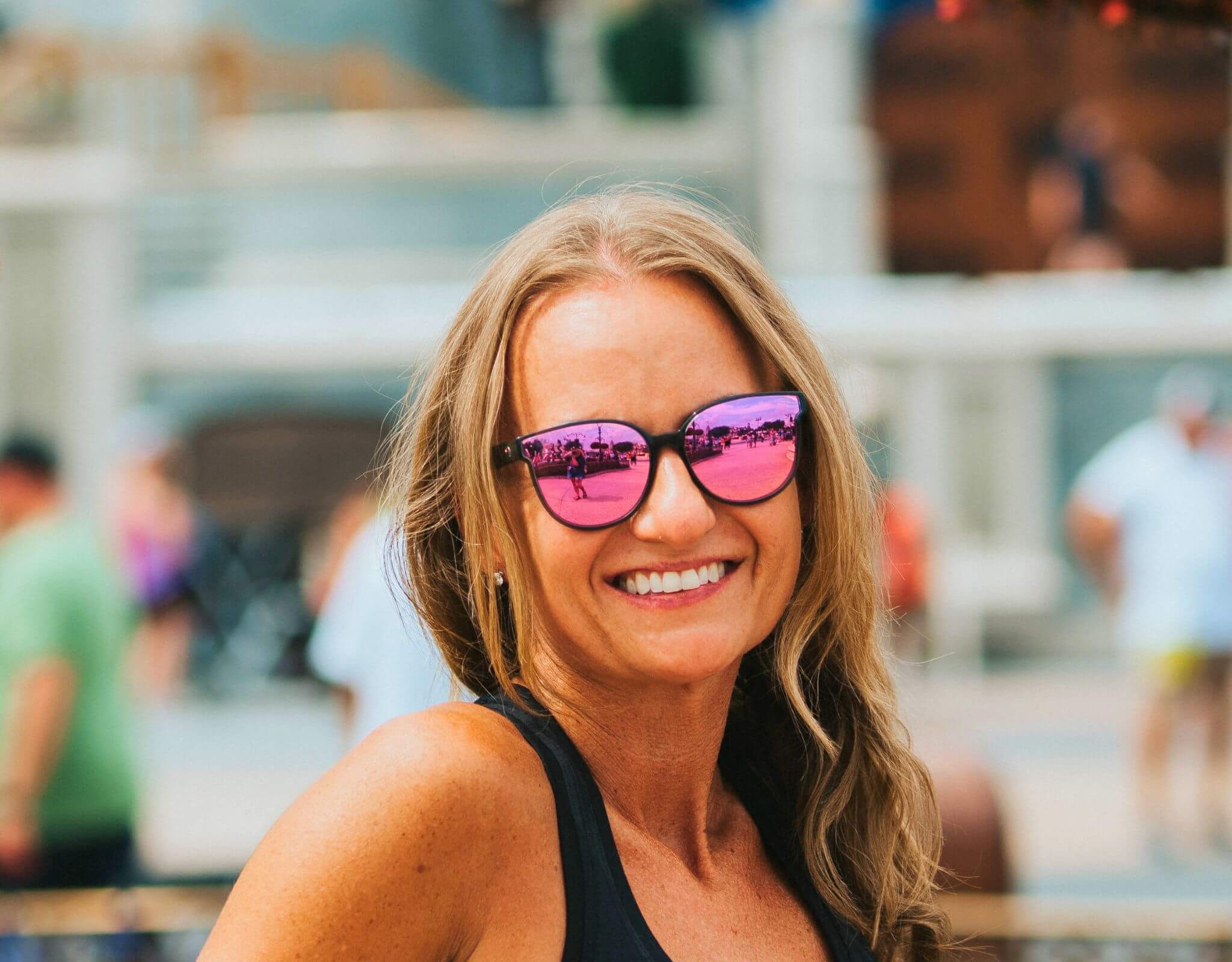 Happy woman wearing grey pink South Beach shades for small faces at a sunny outdoor event.