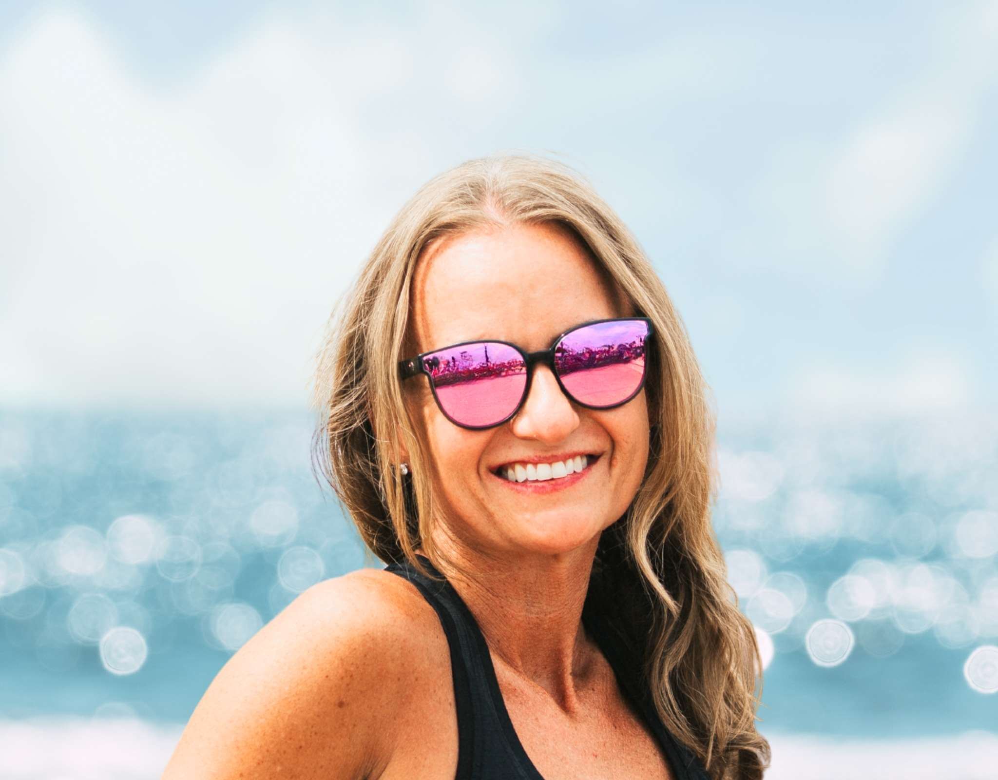 Happy woman wearing grey pink South Beach shades for small faces at a sunny beach.