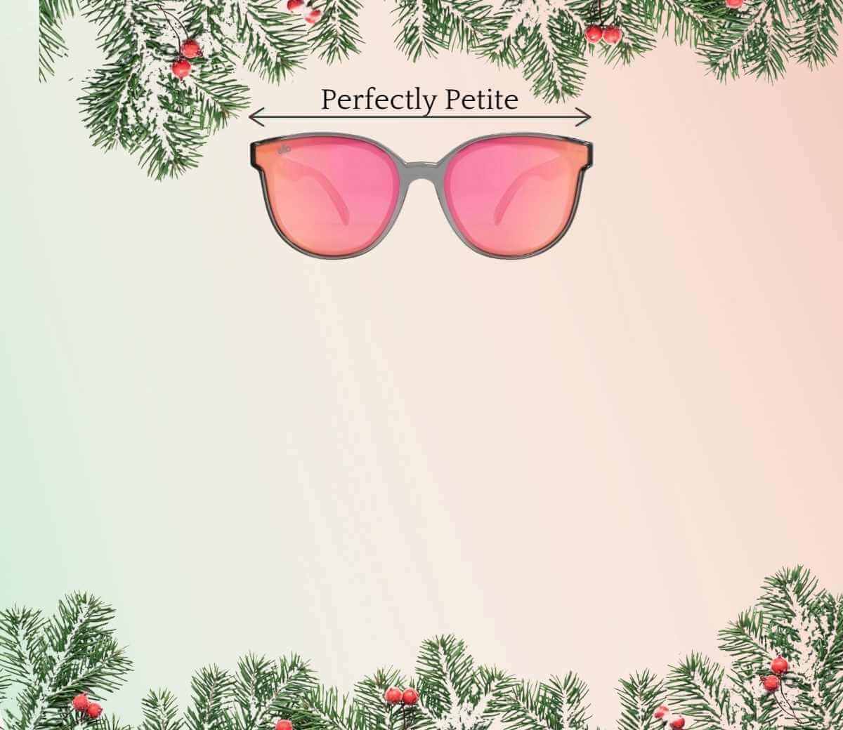Pink sunglasses with 'Perfectly Petite' text surrounded by Christmas tree branches on a gradient background