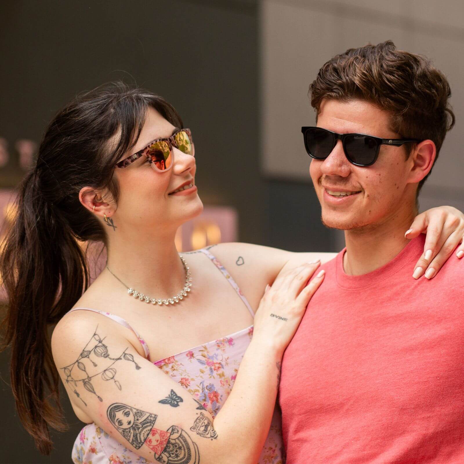 Smiling couple in ello sunglasses for petite faces, sharing a joyful city moment with a confident, sunlit vibe.