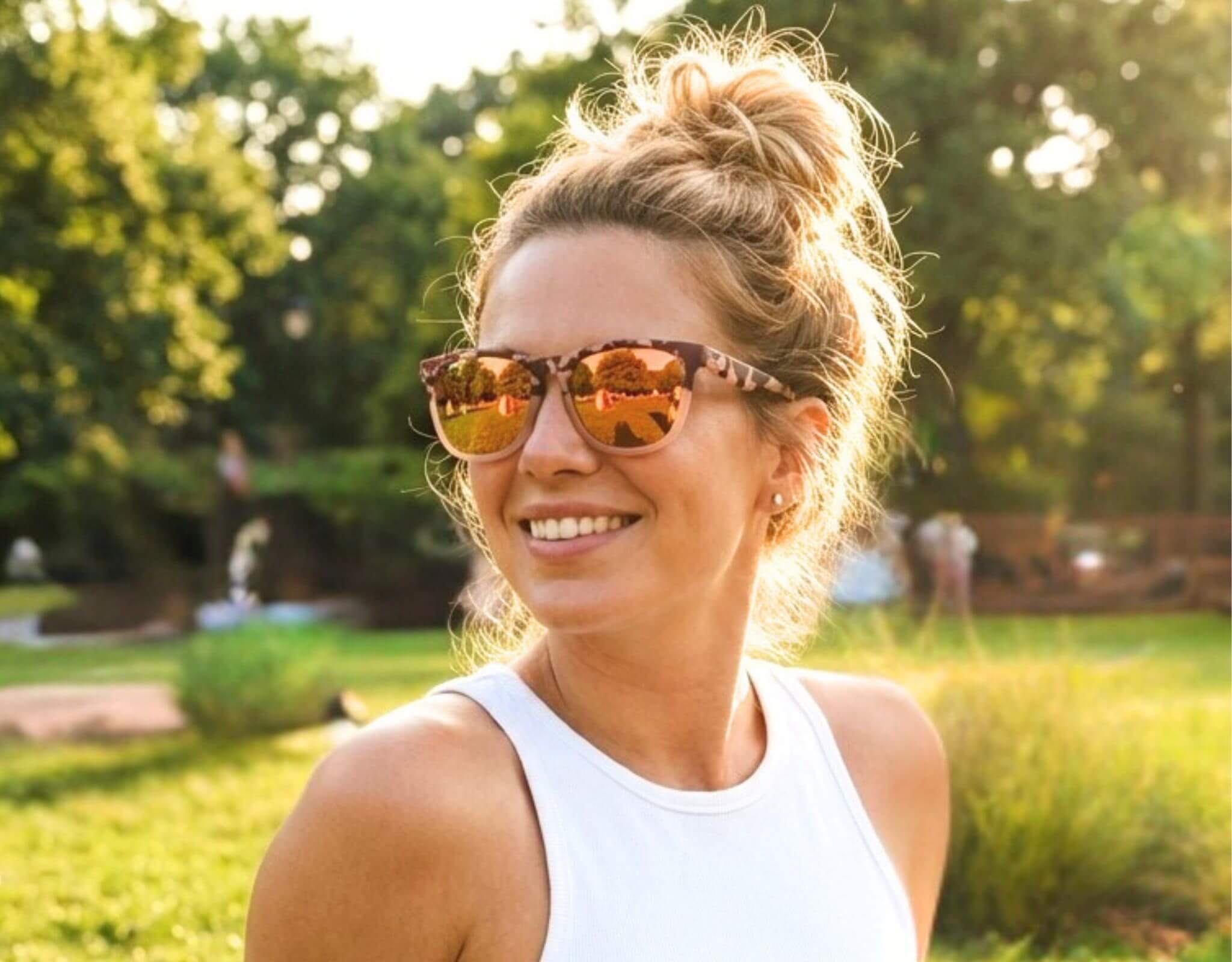 Petite sunglasses for small head worn by woman relaxing in a sunny park, featuring lightweight pink tortoise TR90 ello frames with mirrored lenses in a casual outdoor setting