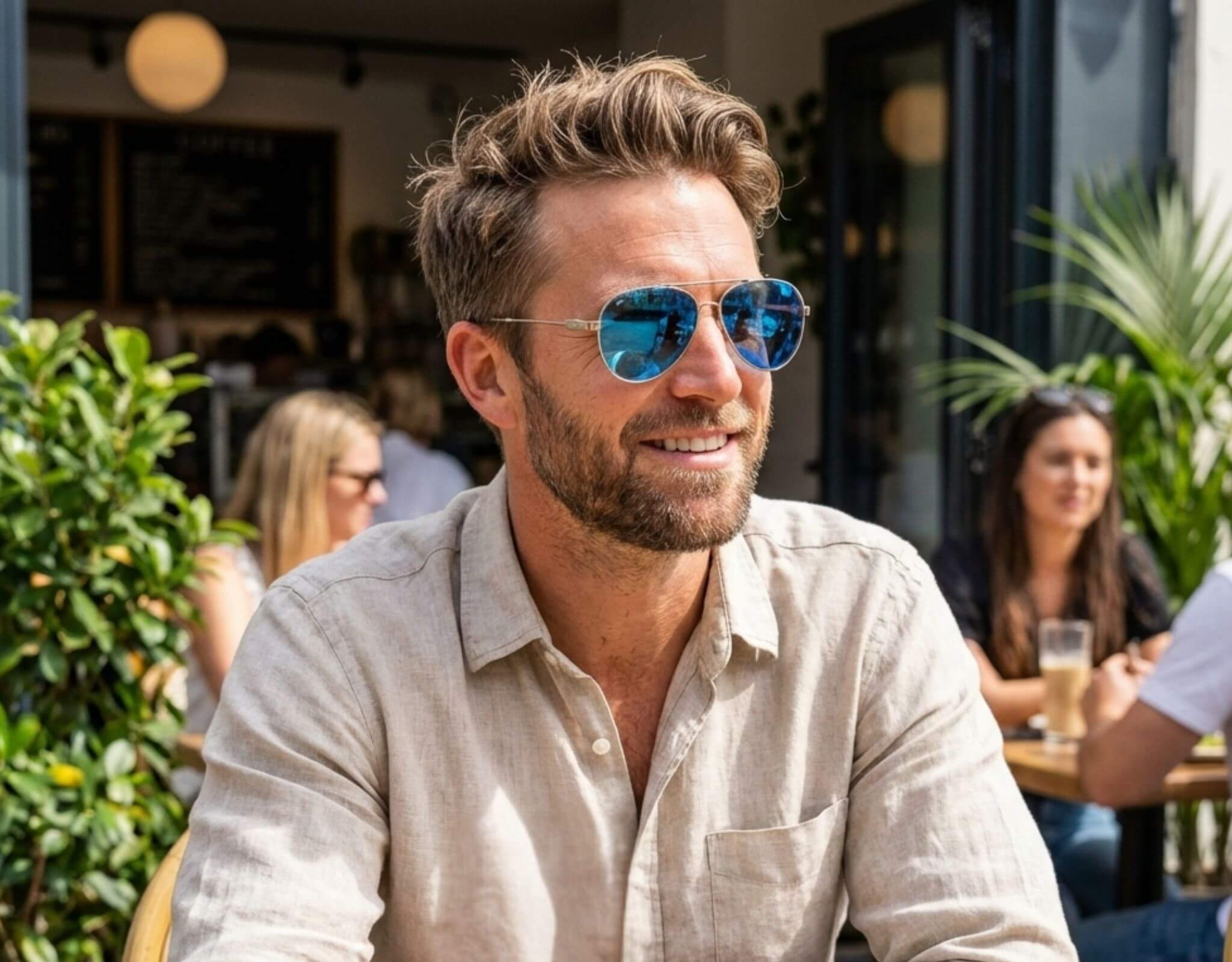 Sunglasses for petite faces worn by man with small head relaxing at an outdoor cafe, featuring lightweight metal aviator ello sunglasses in a bright daytime setting