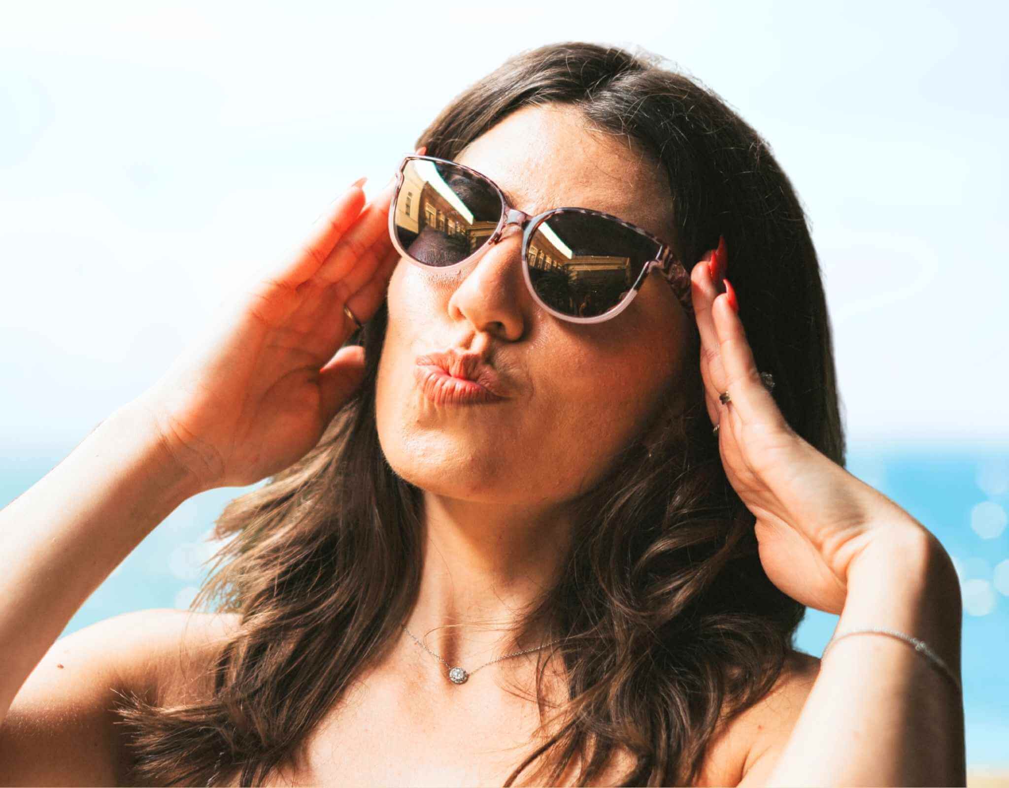 Smiling woman wearing tortoise gold South Beach shades for small faces making a kissy face on the beach.