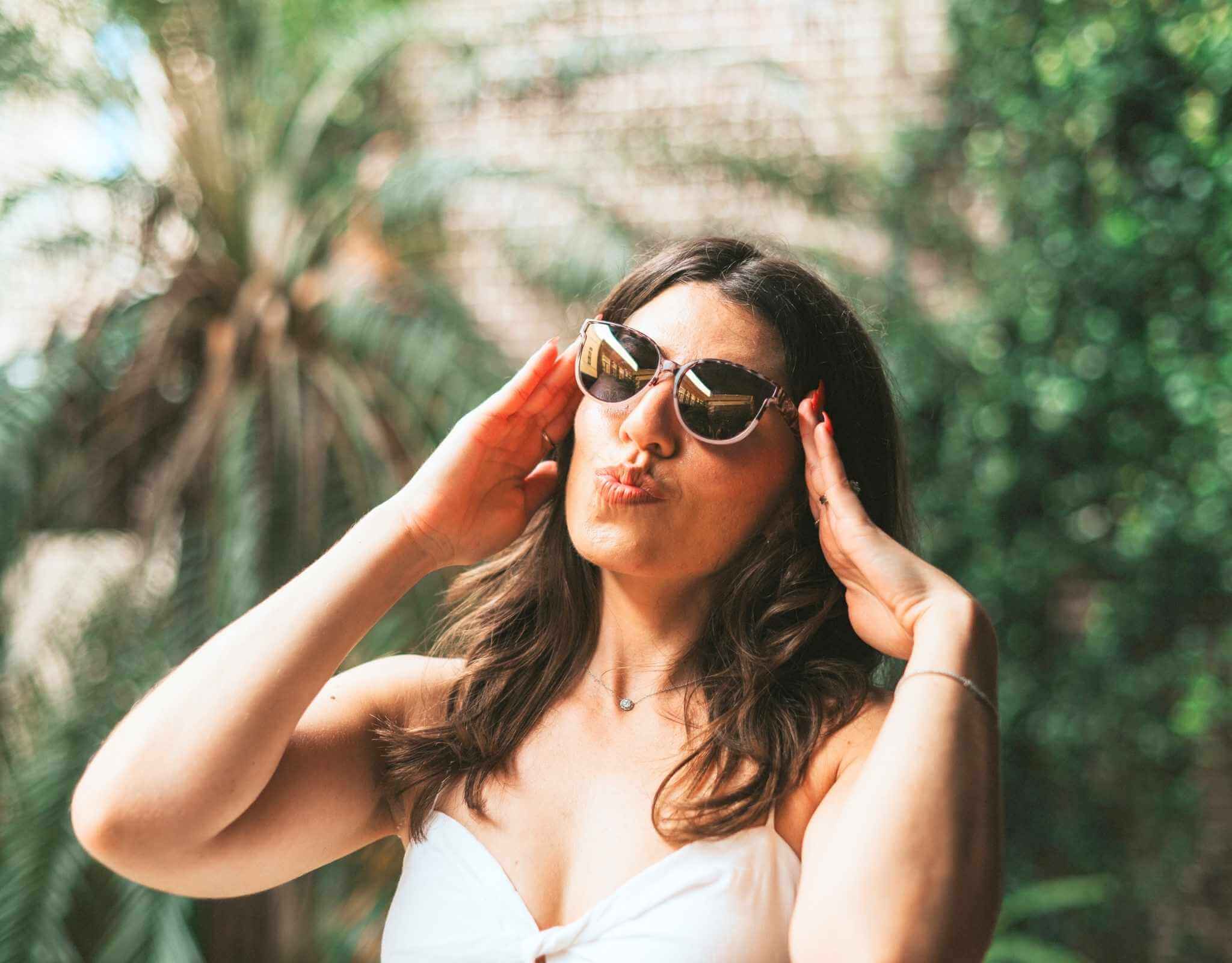 Smiling woman wearing tortoise gold South Beach shades for small faces making a kissy face in a courtyard. 