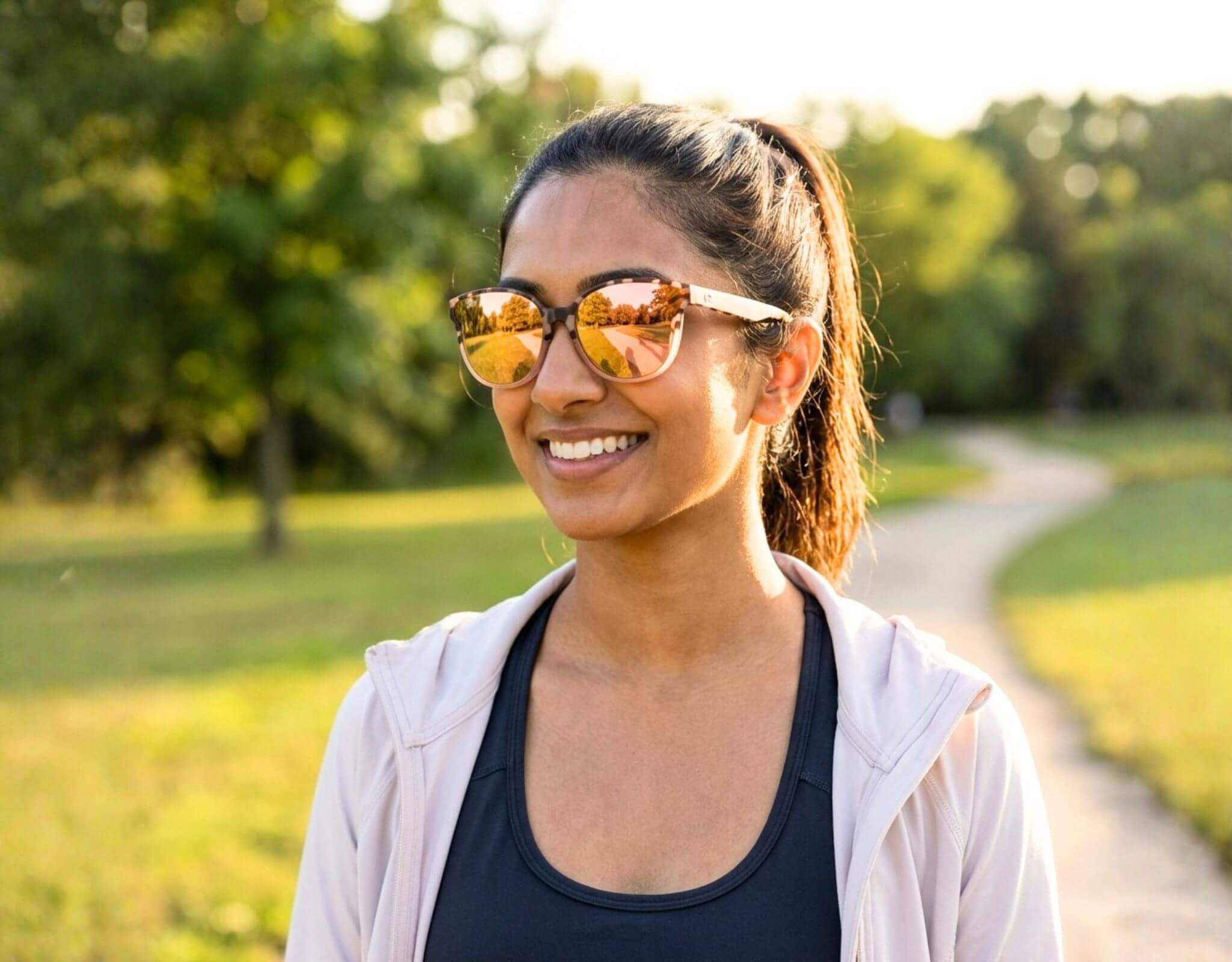 Petite woman with a small head wearing tortoise peach South Beach shades for little faces smiling during a walk in a sunlit park with warm golden reflections